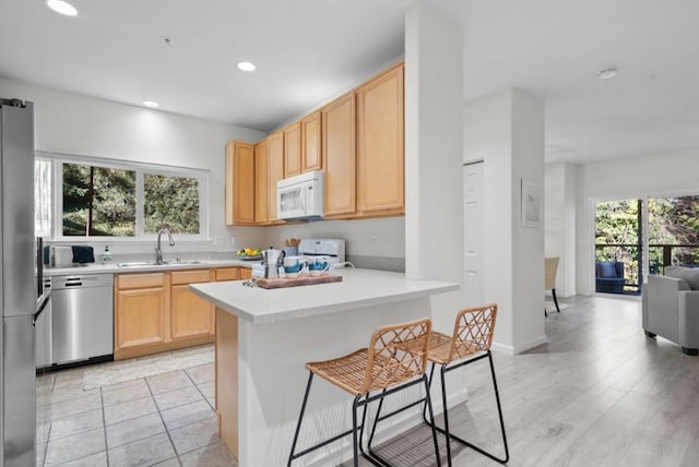 kitchen featuring light brown cabinetry, sink, a breakfast bar area, appliances with stainless steel finishes, and kitchen peninsula