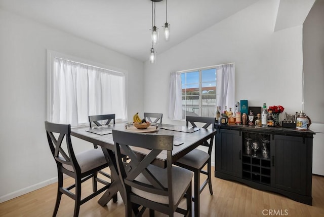 dining space with lofted ceiling, indoor bar, and light hardwood / wood-style flooring