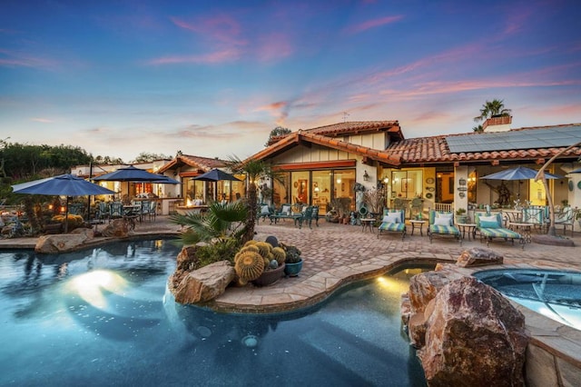 pool at dusk featuring pool water feature and a patio