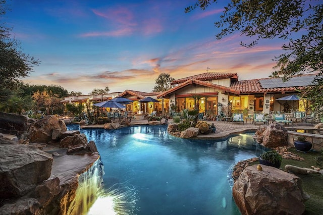 pool at dusk featuring pool water feature and a patio