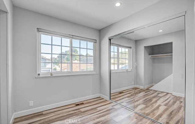 unfurnished bedroom featuring multiple windows, a closet, and light hardwood / wood-style flooring