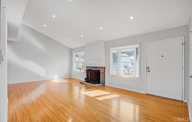 unfurnished living room with plenty of natural light, vaulted ceiling, light hardwood / wood-style flooring, and a brick fireplace