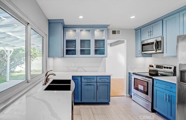 kitchen with light stone counters, sink, blue cabinets, and stainless steel appliances