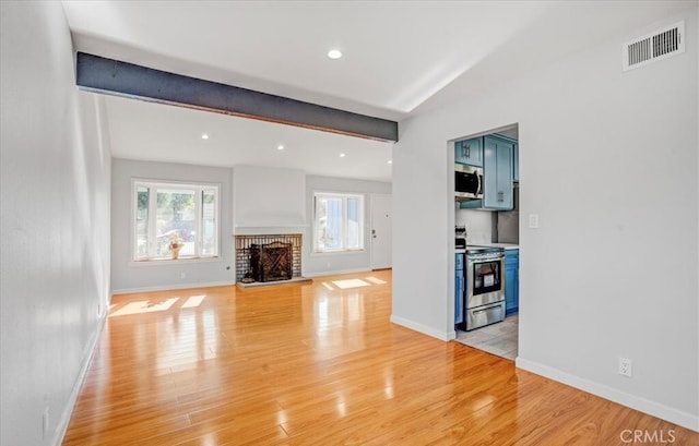 unfurnished living room featuring a fireplace, beamed ceiling, and light hardwood / wood-style flooring