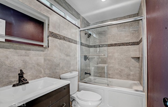 full bathroom featuring combined bath / shower with glass door, vanity, toilet, and tile walls