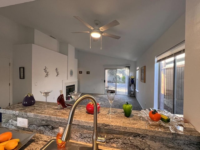 kitchen with a tiled fireplace, ceiling fan, and vaulted ceiling