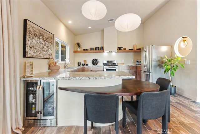 kitchen with pendant lighting, appliances with stainless steel finishes, light stone counters, kitchen peninsula, and beverage cooler