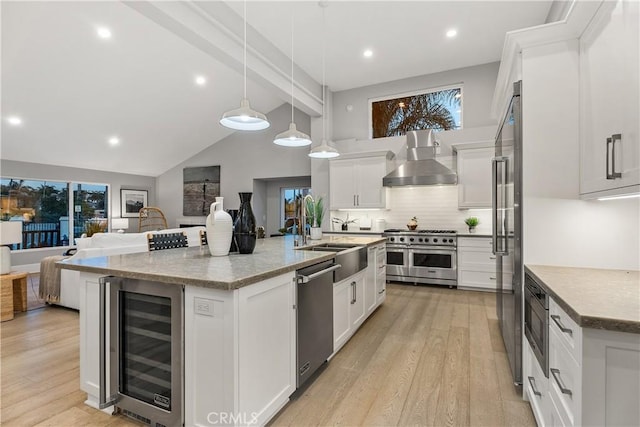 kitchen with an island with sink, stainless steel appliances, wall chimney exhaust hood, and wine cooler