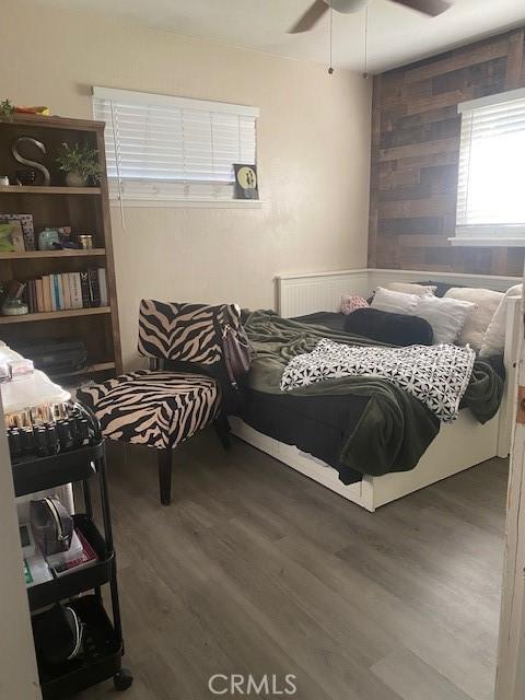 bedroom featuring a ceiling fan, wooden walls, and wood finished floors