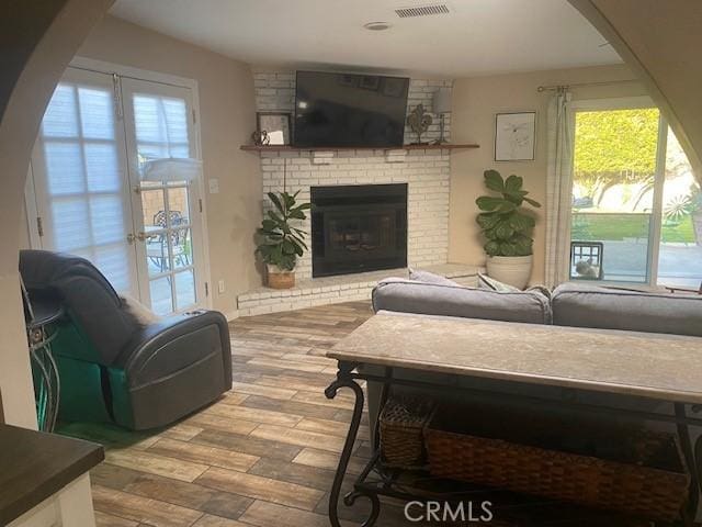 living area featuring a brick fireplace, visible vents, and wood finished floors