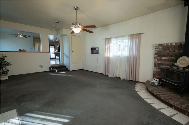 unfurnished living room with dark colored carpet, ceiling fan, and a wood stove