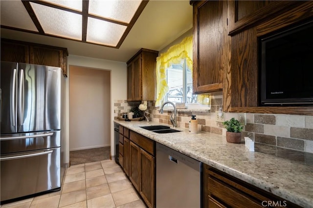 kitchen featuring sink, light tile patterned floors, appliances with stainless steel finishes, backsplash, and light stone counters