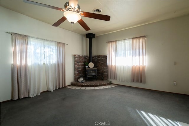 unfurnished living room featuring ceiling fan, carpet floors, and a wood stove