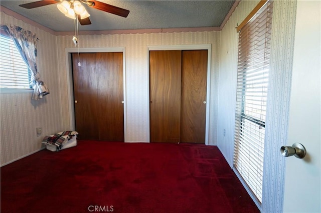 unfurnished bedroom featuring ceiling fan, a textured ceiling, and two closets