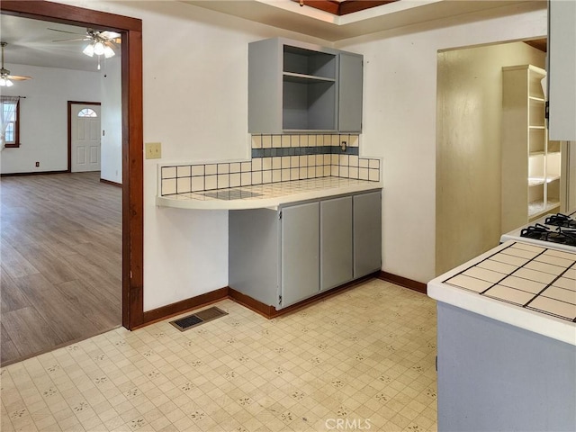 kitchen with ceiling fan, backsplash, gray cabinets, and tile counters