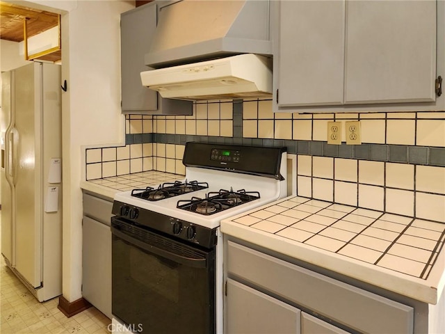 kitchen featuring range hood, white refrigerator with ice dispenser, tile counters, and gas range