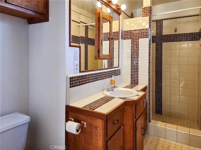 bathroom with backsplash, toilet, tiled shower, and vanity