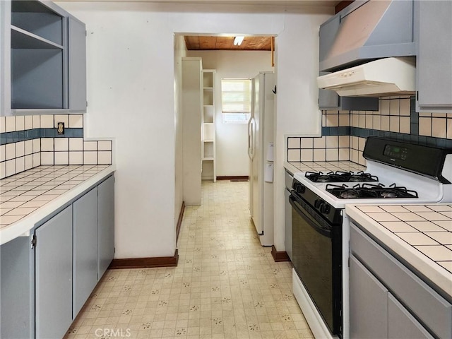 kitchen featuring white refrigerator with ice dispenser, gas range, backsplash, gray cabinets, and tile counters