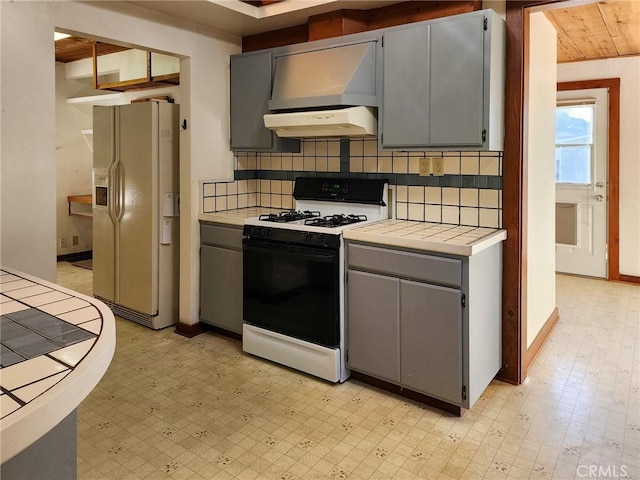 kitchen featuring gas range oven, gray cabinets, white fridge with ice dispenser, and tile countertops