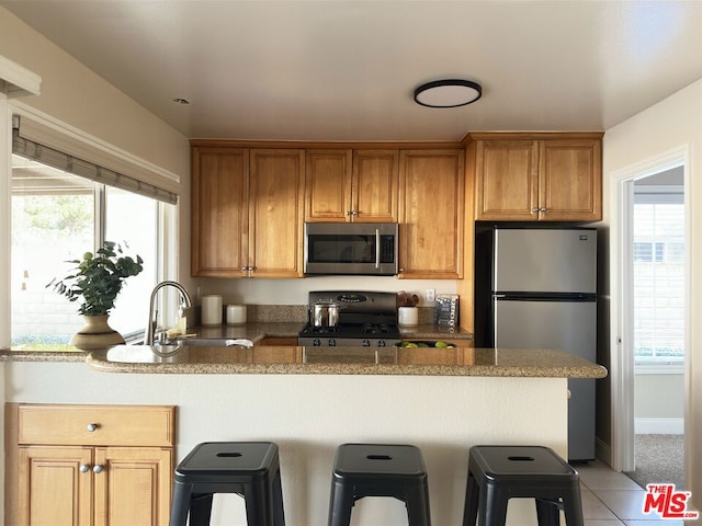 kitchen with appliances with stainless steel finishes, light tile patterned floors, a breakfast bar area, and sink