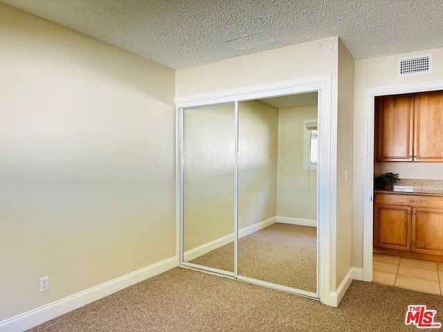 unfurnished bedroom featuring a textured ceiling, carpet floors, and a closet