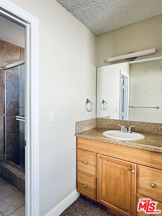 bathroom with vanity, a shower with shower door, and a textured ceiling