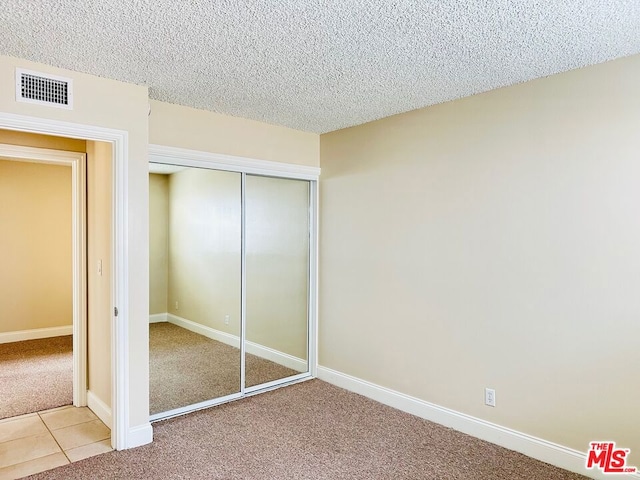 unfurnished bedroom featuring a textured ceiling, light colored carpet, and a closet