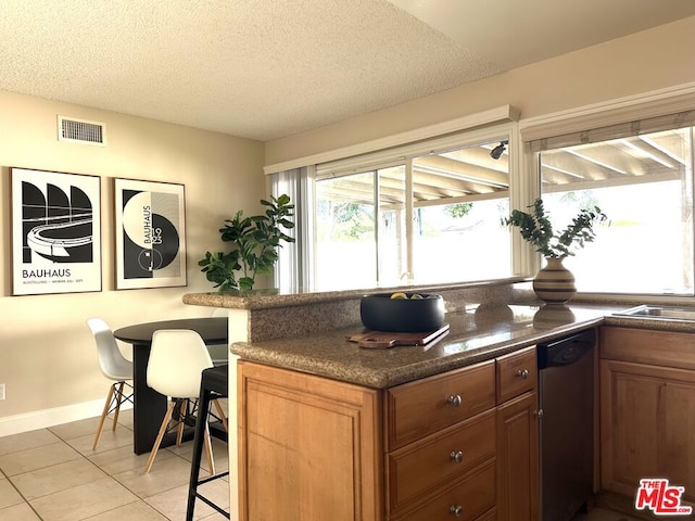 kitchen with stainless steel dishwasher, sink, light tile patterned floors, and a textured ceiling