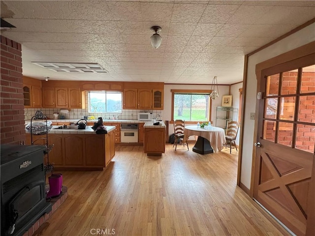 kitchen featuring light wood-type flooring, backsplash, white appliances, crown molding, and hanging light fixtures