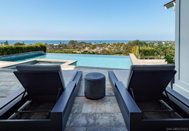 view of pool featuring an in ground hot tub, a water view, and a patio area