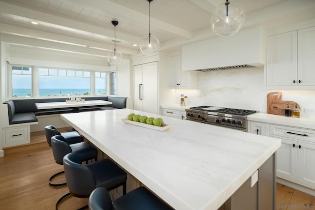 kitchen featuring pendant lighting, white cabinets, a water view, beamed ceiling, and range