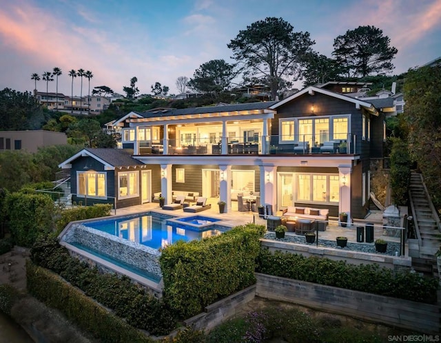 back house at dusk with a swimming pool with hot tub, a balcony, an outdoor hangout area, and a patio area