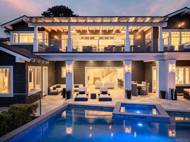 back house at dusk with an outdoor living space, a balcony, a patio, and a pool with hot tub