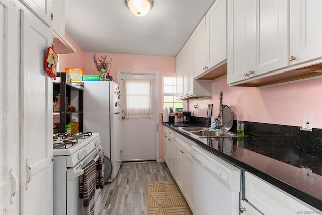 kitchen with white appliances, dark stone counters, white cabinets, sink, and light wood-type flooring