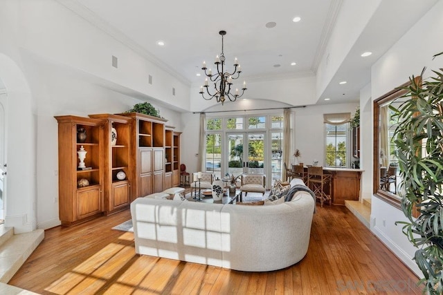 living room with french doors, light hardwood / wood-style flooring, a towering ceiling, a chandelier, and ornamental molding