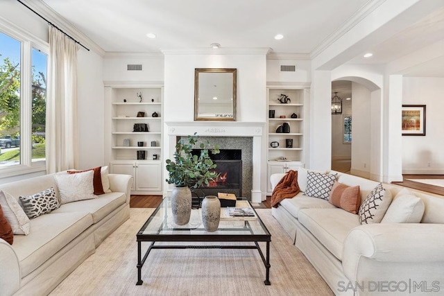 living room with light wood-type flooring, built in features, a healthy amount of sunlight, and crown molding