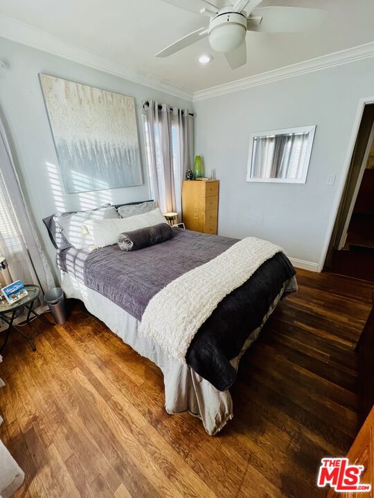 bedroom with hardwood / wood-style flooring, ornamental molding, and ceiling fan