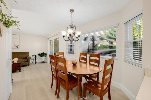 dining space with light hardwood / wood-style floors, a textured ceiling, and an inviting chandelier