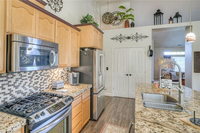 kitchen with sink, hanging light fixtures, light stone counters, backsplash, and appliances with stainless steel finishes