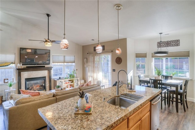 kitchen with light stone countertops, sink, hanging light fixtures, a kitchen island with sink, and hardwood / wood-style flooring