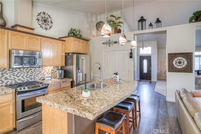 kitchen featuring sink, a high ceiling, light stone counters, a kitchen island with sink, and appliances with stainless steel finishes