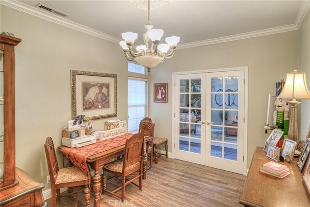 dining space featuring hardwood / wood-style floors, crown molding, french doors, and a chandelier