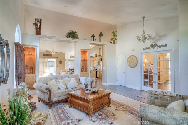 living room featuring a towering ceiling, french doors, ceiling fan with notable chandelier, and hardwood / wood-style flooring