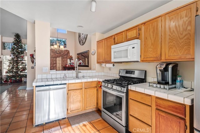 kitchen with tile countertops, an inviting chandelier, sink, light tile patterned floors, and stainless steel appliances