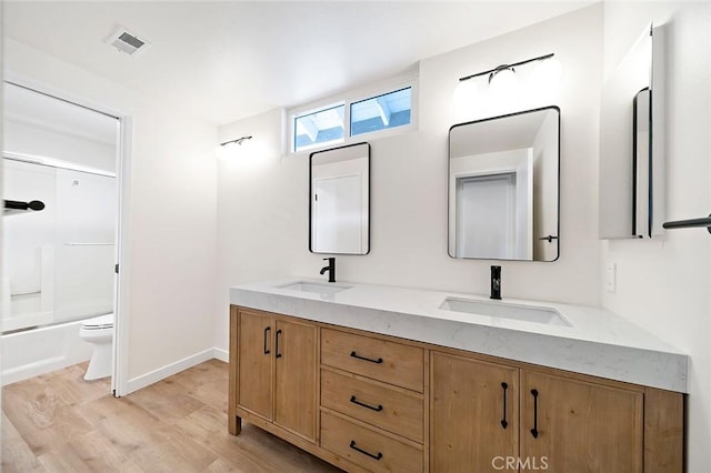 full bathroom with combined bath / shower with glass door, wood-type flooring, vanity, and toilet