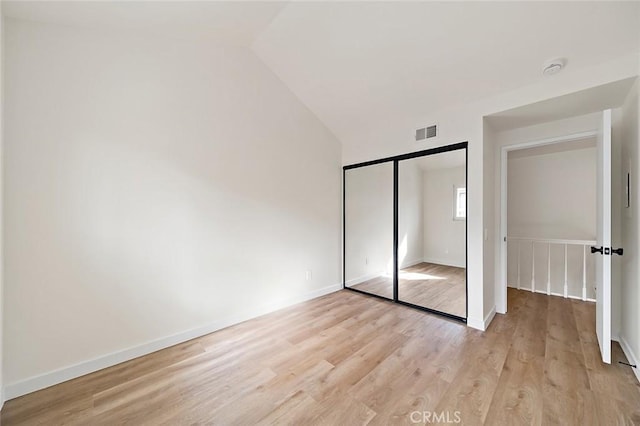 unfurnished bedroom featuring light wood-type flooring, vaulted ceiling, and a closet