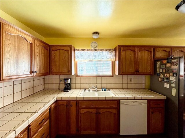 kitchen with tile counters, backsplash, stainless steel fridge, and white dishwasher