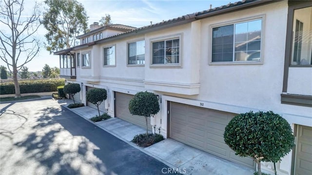 view of side of property with driveway, an attached garage, a chimney, and stucco siding