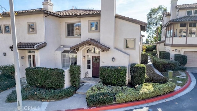 mediterranean / spanish-style home featuring a tile roof, a chimney, and stucco siding