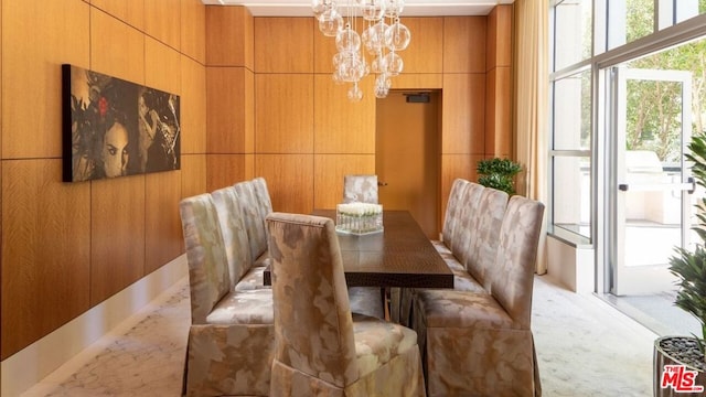 dining area with light carpet, a notable chandelier, and wooden walls